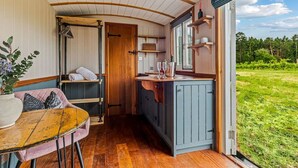 Een gezellig interieur van een chalet, met een houten plafond, een eethoek met tafel en stoelen, een kitchenette en een groot raam met uitzicht op de natuur.