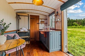 Ein gemütliches Blockhaus-Interieur mit Holzbalkendecke, einem Essbereich mit Tisch und Stühlen, einer Küchenzeile und einem großen Fenster mit Blick ins Freie.