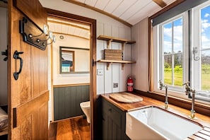 A compact kitchen with wooden cabinetry, a sink, a window with a view of greenery, and a fire extinguisher. - Golden Grape in Oakengrove Vineyard (Buckinghamshire)