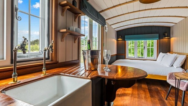 Een kamer met houten vloer, een groot raam, een bed, een tafel en een wastafel.