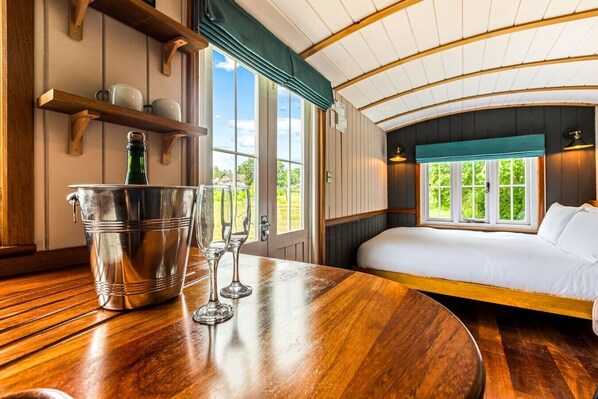 Ein Zimmer mit Holztisch, einem Bett mit weißer Bettwäsche und Blick auf Grünfläche.