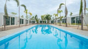 A swimming pool with a clear blue surface, surrounded by modern buildings and palm trees.