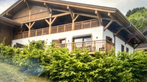 Een gebouw met twee verdiepingen en een balkon, omringd door groen.