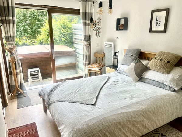A bedroom with a bed, pillows, a nightstand, a chair, a window with curtains, and a view of greenery outside. - Apartment Le Rouge Gorge (Les Gets)