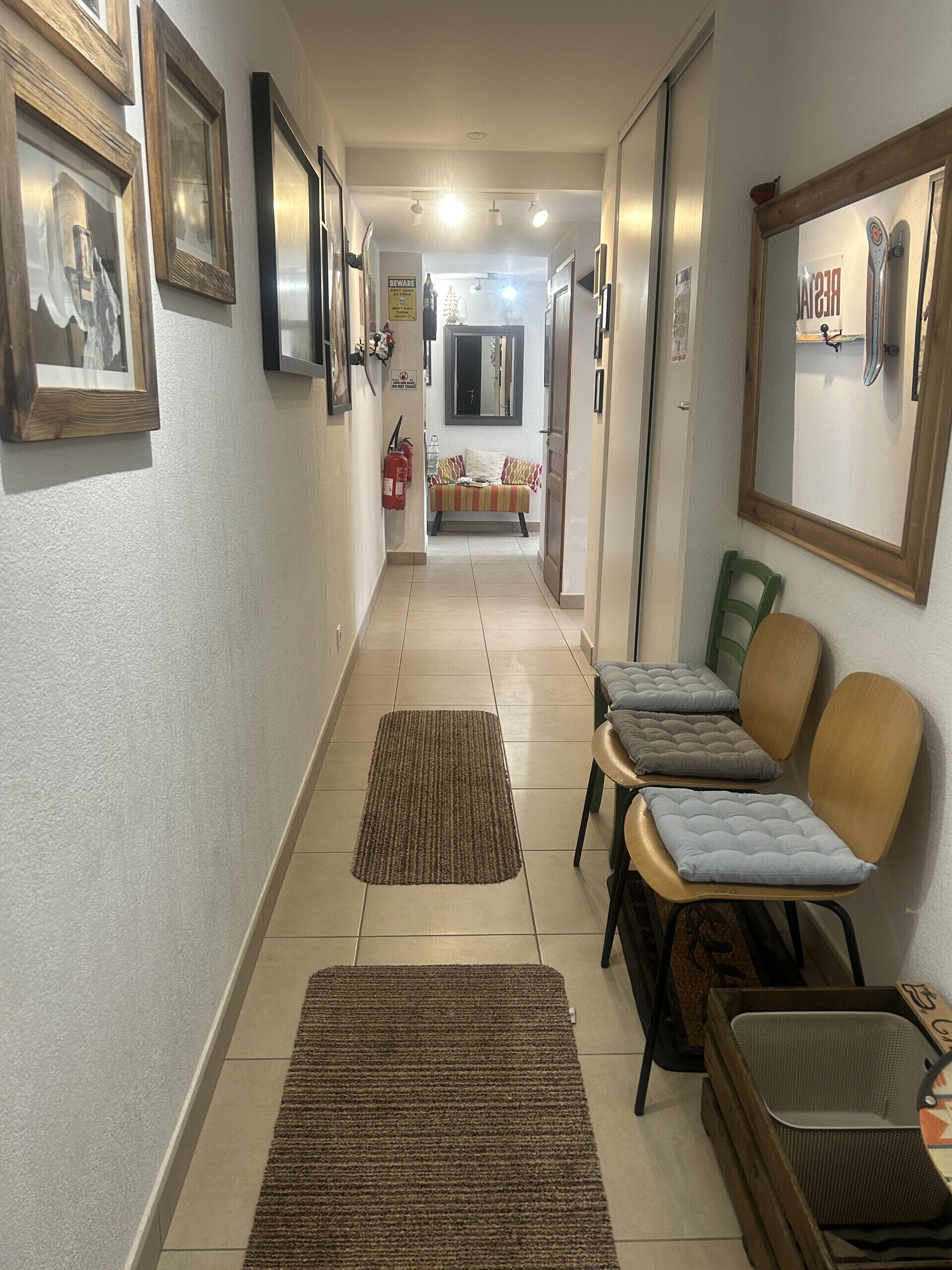A hallway with framed pictures, a sofa, chairs, and a fire extinguisher.