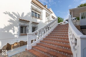 A white building with a staircase leading to a covered area, featuring patterned tiles and metal railings. - Villa SAO PAULO by Abahana Villas (Moraira)