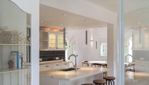 A modern kitchen with white cabinetry, a central island with stools, and a dining area with a table and chairs. - Villa SAO PAULO by Abahana Villas (Moraira)