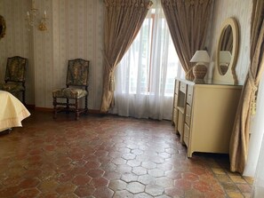 A room with a hexagonal tiled floor, a chair, a dresser, a mirror, and a window with curtains.