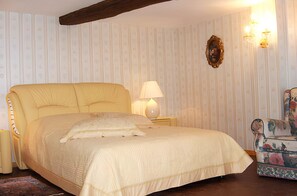 A bed with a headboard, a bedside lamp, a floral armchair, and a wall with vertical stripes.
