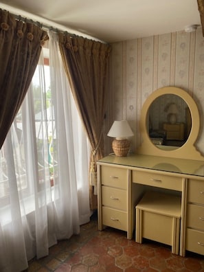 A room with a vanity, a mirror, a lamp, and curtains. - Le Relais Des Hirondelles – Camélia Room with Private Garden (Chaumont-en-Vexin)