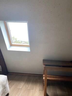 A room with a sloped ceiling, a skylight, a wooden bench, and a patterned rug. - Le Relais Des Hirondelles B&B – Gardénia Room with Private Garden (Chaumont-en-Vexin)