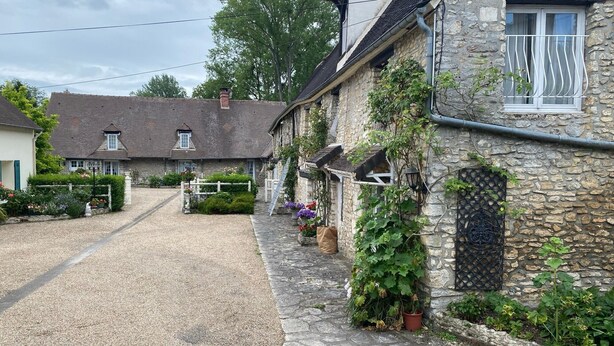 Ein Steinhaus mit Kiesauffahrt, einem weißen Zaun und einem kleinen Garten mit Blumen.