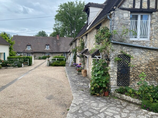 Ein Steinhaus mit Kiesauffahrt, einem weißen Zaun und einem kleinen Garten mit Blumen.
