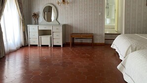 Ein Schlafzimmer mit weißem Schminktisch, einem runden Spiegel, einer Holzbank und einem Bett.