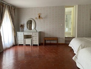 Ein Schlafzimmer mit weißem Schminktisch, einem runden Spiegel, einer Holzbank und einem Bett.