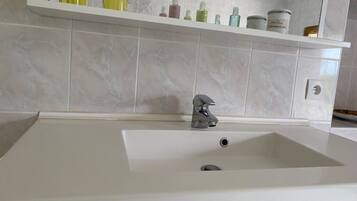 A bathroom with a white sink, a mirror, and a shelf with toiletries.