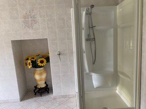 Ein Badezimmer mit einer Duschkabine, Fliesenboden und einer Vase mit Sonnenblumen auf einem Sockel.