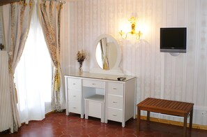 Ein Zimmer mit weißem Schminktisch, einer Holzbk, einem an der Wand montierten Fernseher und einem Spiegel.