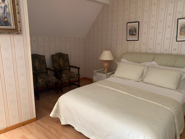 A bedroom with a large bed, two chairs, a nightstand with a lamp, and framed pictures on the wall. - Le Relais Des Hirondelles - Magnolia Room with Private Garden (Chaumont-en-Vexin)