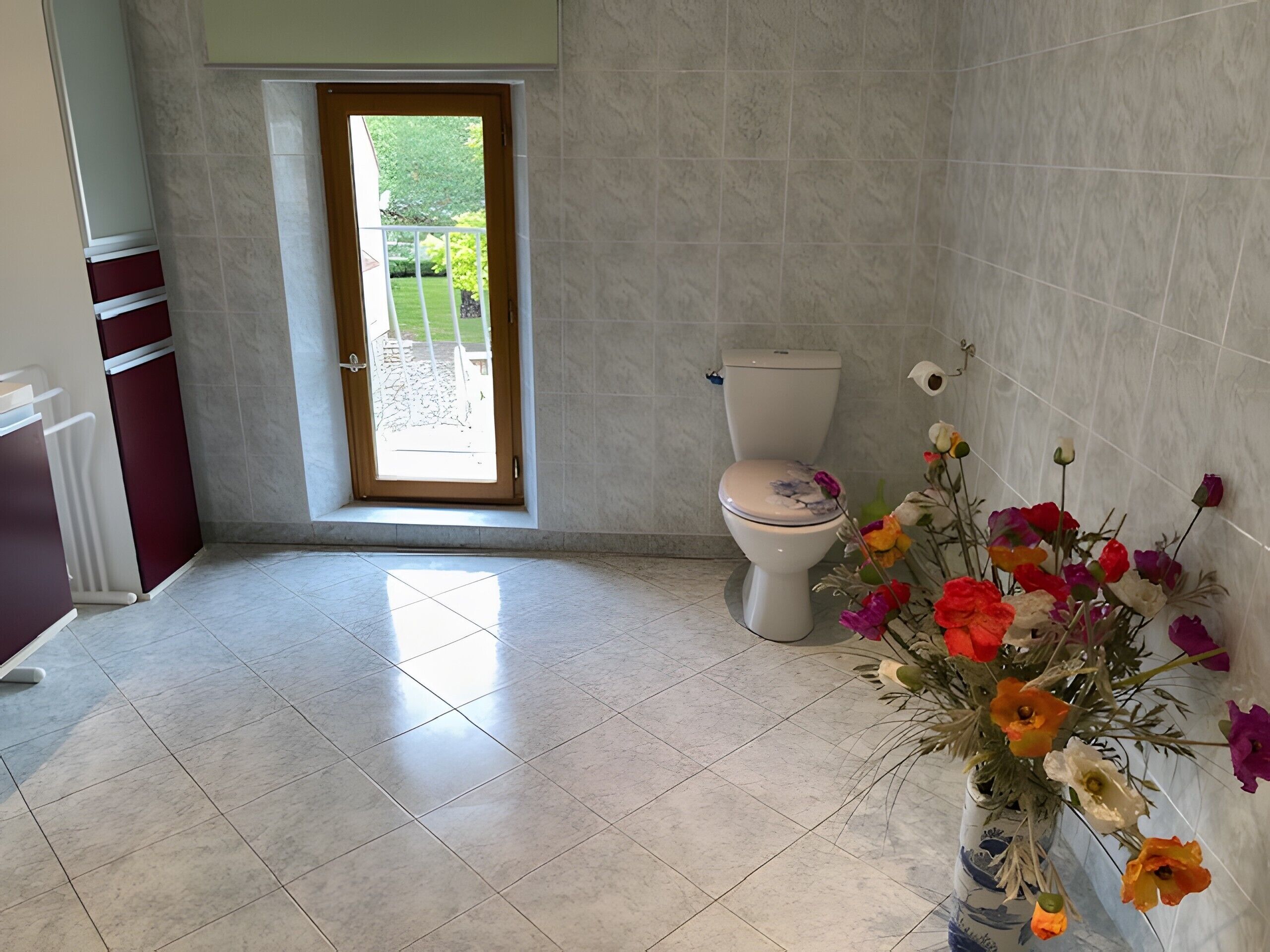 Een badkamer met een toilet, een raam en een bloevas.