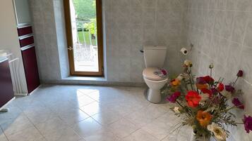 Een badkamer met een toilet, een raam en een bloevas.