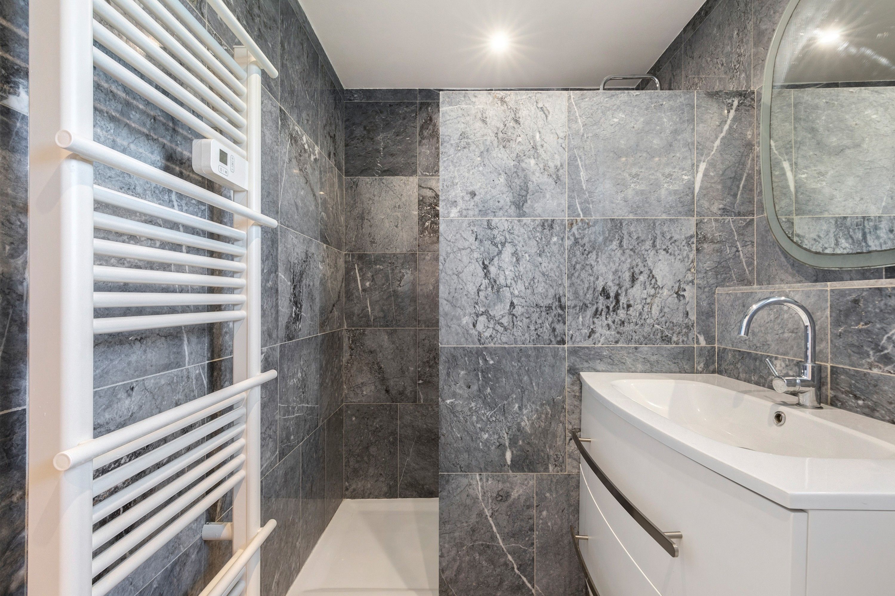 Ein modernes Badezimmer mit einer weißen Badewanne, einem weißen Handtuchhalter und einem Spiegel über dem Waschbecken.