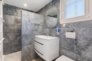 A modern bathroom with a white vanity, a mirror, and a shower area.