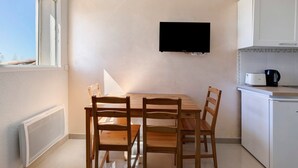 Une petite cuisine avec une table et des chaises, un téléviseur fixé au mur et une fenêtre qui laisse entrer la lumière naturelle.
