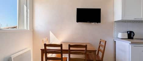Una cocina pequeña con una mesa de comedor y sillas, un televisor montado en la pared y un ventanal que proporciona luz natural.