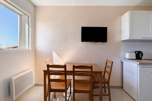 A small kitchen with a dining table and chairs, a television mounted on the wall, and a window providing natural light.