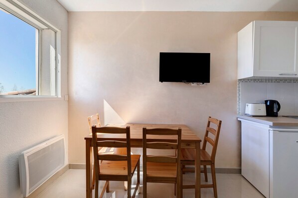 A small kitchen with a dining table and chairs, a television mounted on the wall, and a window providing natural light.
