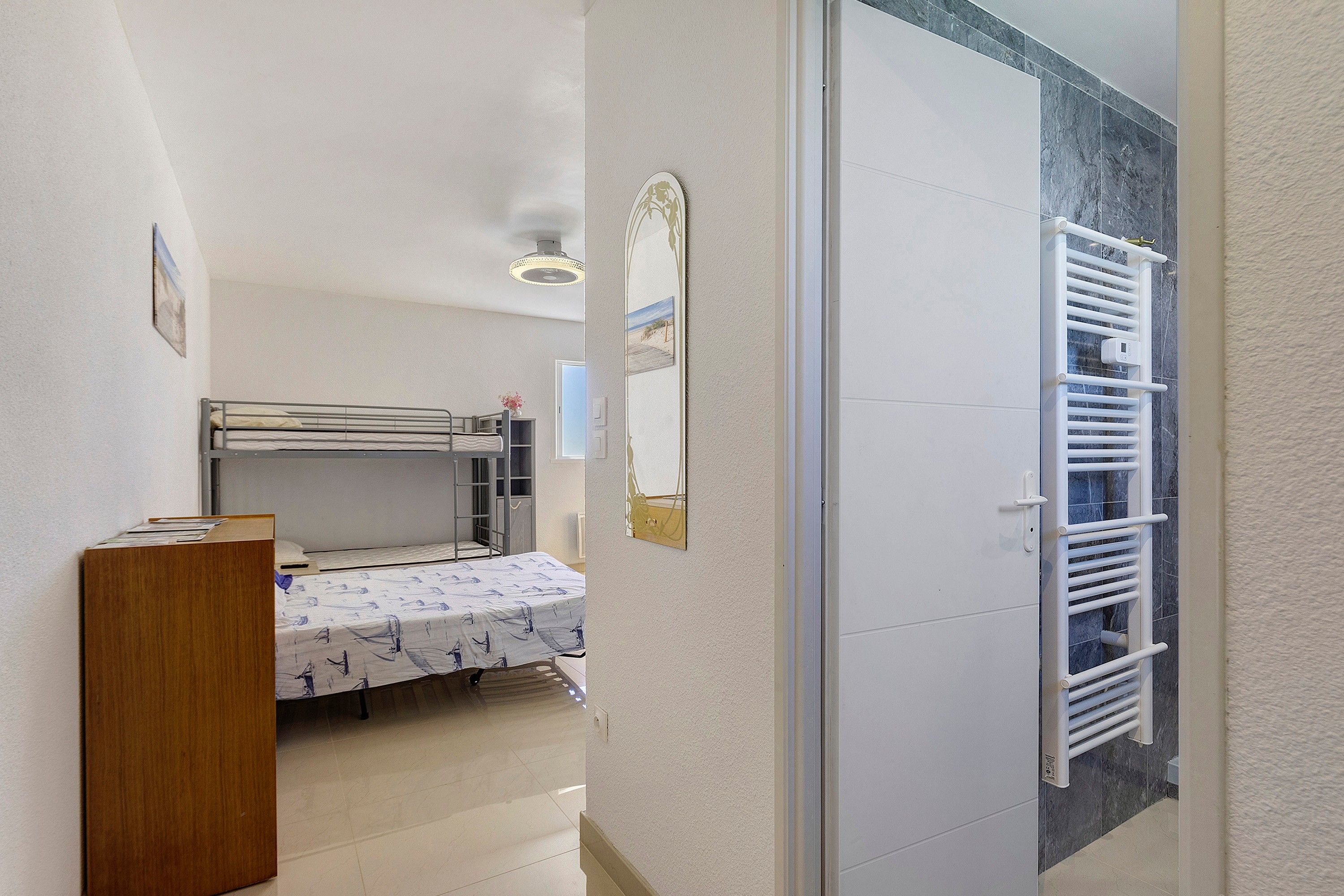 Een kleine kamer met een stapelbed, een houten kast, een spiegel en een radiator.
