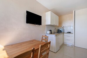A compact kitchen with a wooden table and chairs, a flat-screen TV mounted above the counter, and a microwave. - Ceraria Apartment with Shared Pool (Loupian)