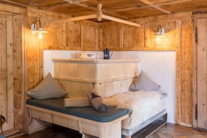 A wooden cabin interior with a stone bench, pillows, a fur throw, and a coffee pot. - Ferienhaus Victoria in Schruns (Schruns)