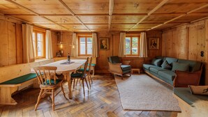 Interior de una cabaña de madera con una mesa de comedor, sillas, un sofá y una chimenea.