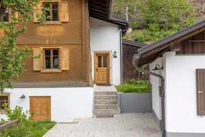 A two-story house with a wooden door, a welcome mat, and a staircase leading to the entrance. - Ferienhaus Victoria in Schruns (Schruns)