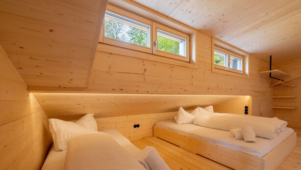 Una cabaña de madera con dos camas, techo inclinado y dos ventanas.