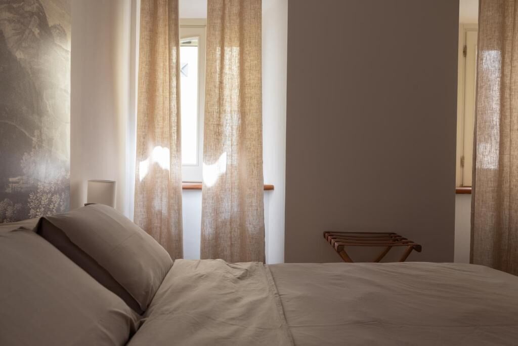 Ein Schlafzimmer mit einem Bett, Vorhängen, einem Nachttisch und einem Holzstuhl.