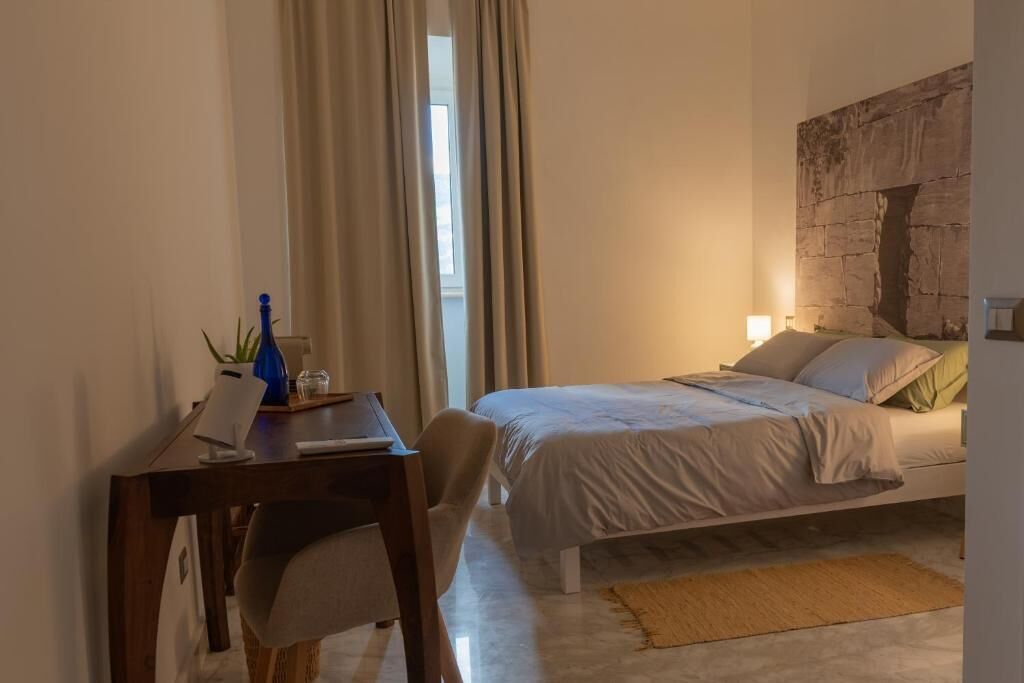 Ein Schlafzimmer mit einem Bett, einem Schreibtisch, einem Stuhl, einem Fenster mit Vorhängen und einem Wandbild.