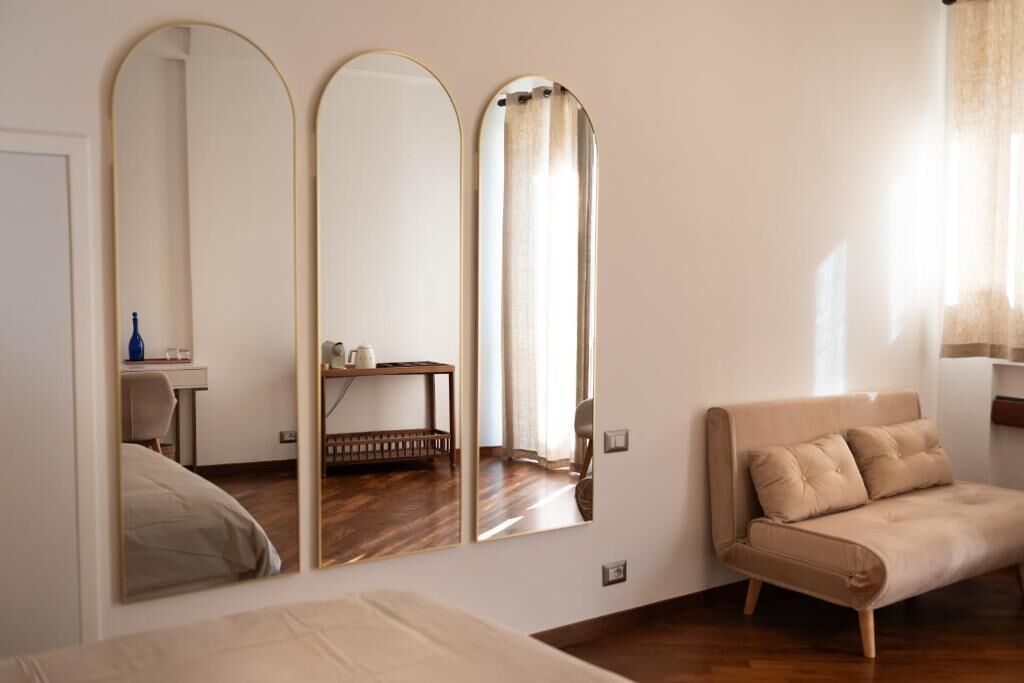 A room with a bed, a sofa, and three mirrors on the wall.