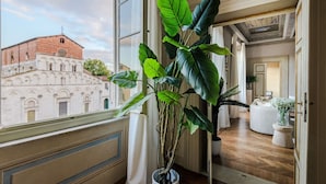 Ein Zimmer mit großem Fenster, einem Blumentopf und Blick auf ein historisches Gebäude.
