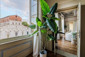 Ein Zimmer mit großem Fenster, einem Blumentopf und Blick auf ein historisches Gebäude.