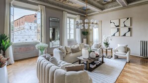 Ein geräumiges Wohnzimmer mit hoher Decke, großen Fenstern und Blick auf ein historisches Gebäude.