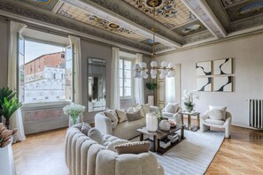 Ein geräumiges Wohnzimmer mit hoher Decke, großen Fenstern und Blick auf ein historisches Gebäude.