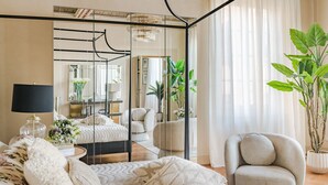 Ein Schlafzimmer mit Bett, Sessel, Spiegel, Lampe und einem Blumentopf.