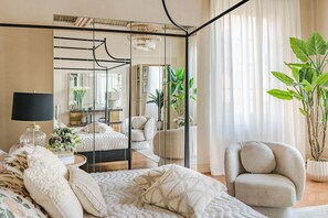Ein Schlafzimmer mit Bett, Sessel, Spiegel, Lampe und einem Blumentopf.