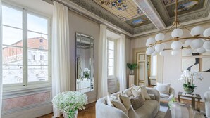 Ein geräumiges Zimmer mit großem Fenster, einer Couch, einem Spiegel und einer Kristallleuchtre.