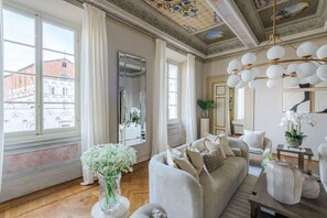 Ein geräumiges Zimmer mit großem Fenster, einer Couch, einem Spiegel und einer Kristallleuchtre.