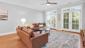 A living room with a brown leather sofa, a coffee table, a lamp, and a ceiling fan. - Sleeps 18, 3 Suites | Walkable Historic District | The Juliette by AvantStay (Savannah)