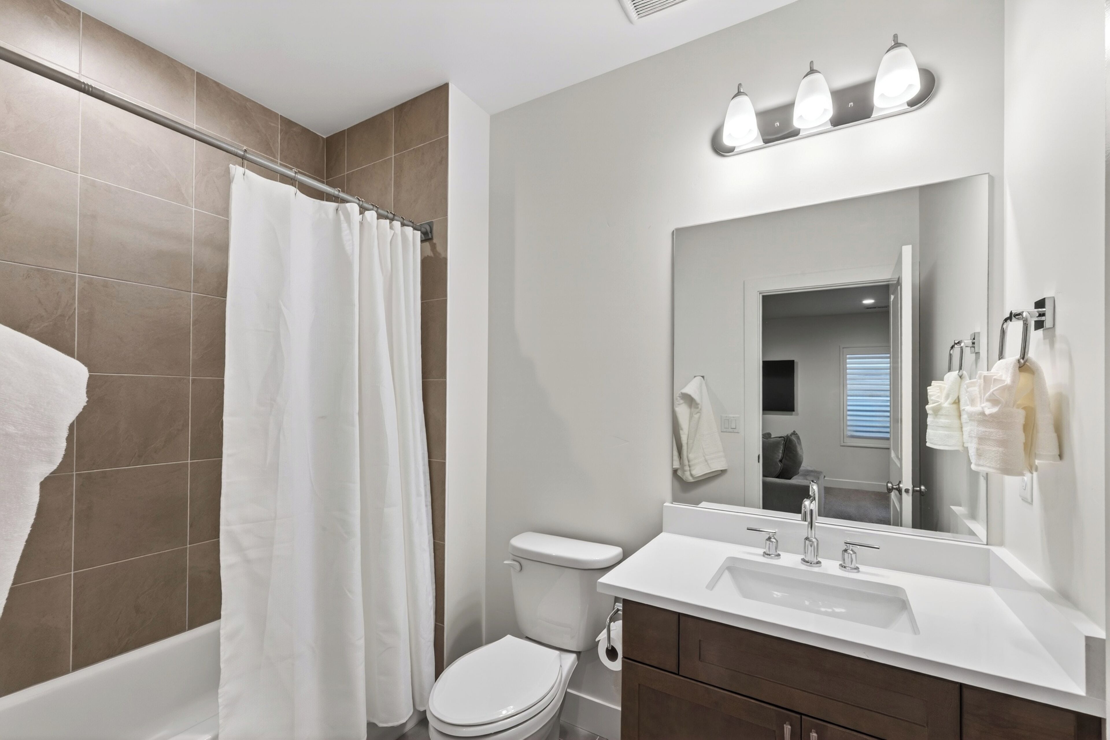 A bathroom with a shower curtain, toilet, sink, and mirror.